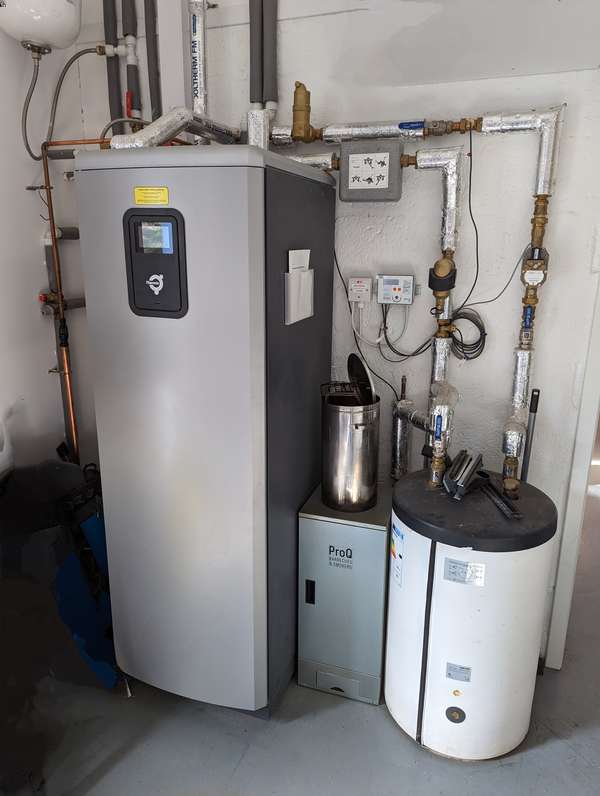 A large, grey, upright box with electrical cabling, plus water tanks and pipes to the right of it